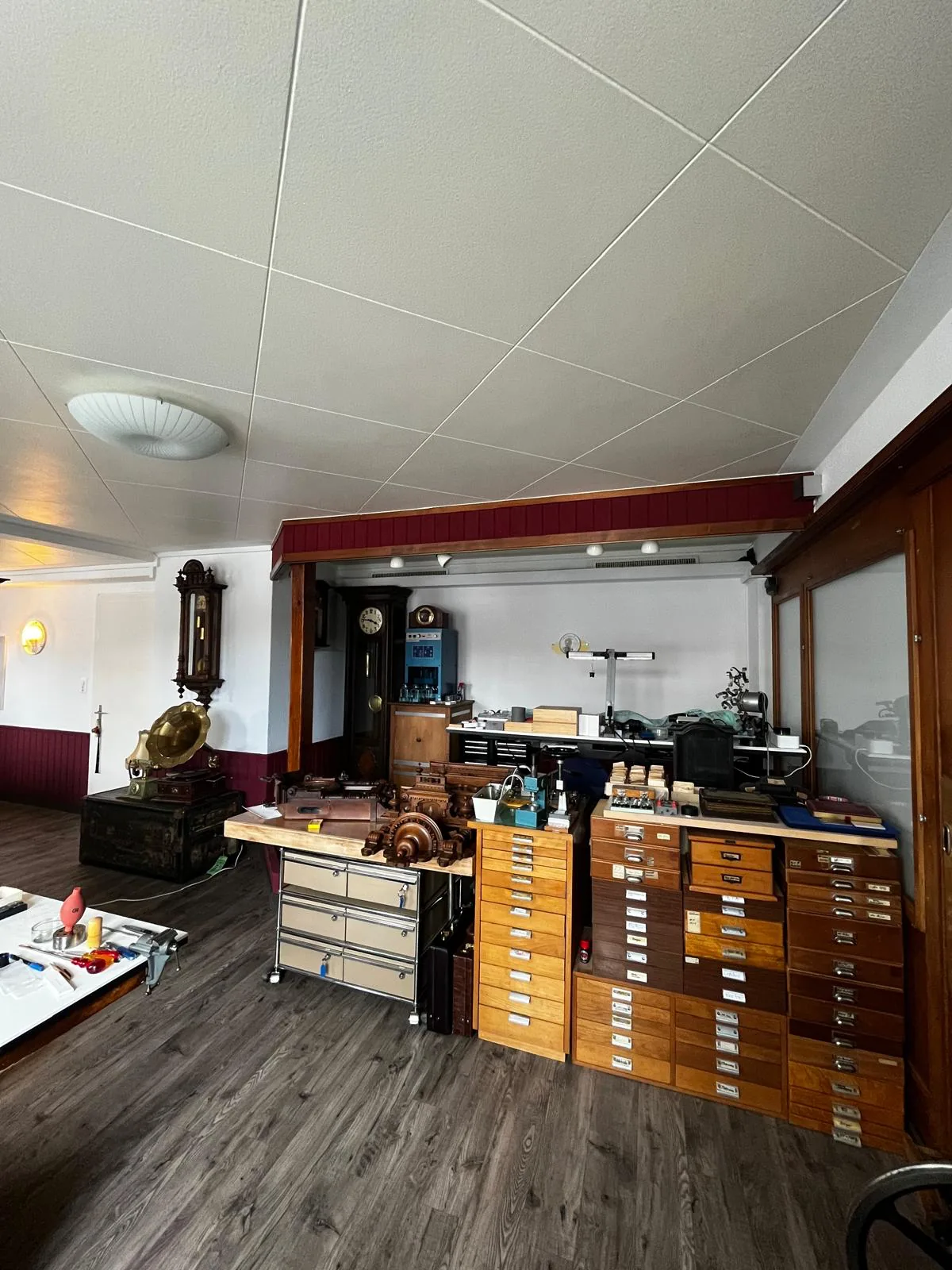 Werkstatt-Übersicht im Atelier Hellmüller Eglisau mit Schubladenkommoden, Drehbank und Standuhren